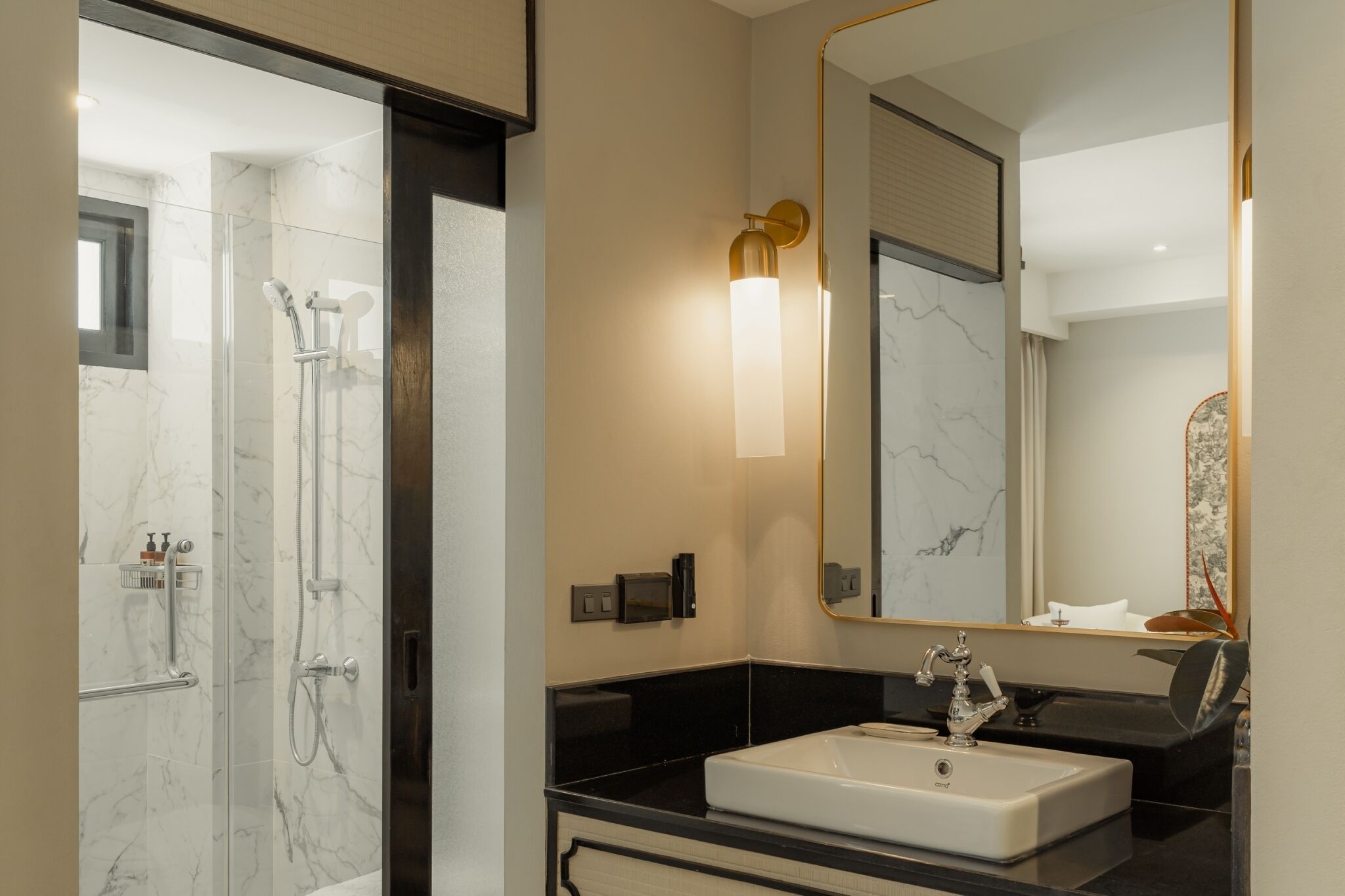 Un baño moderno con ducha envuelta en vidrio, un lavabo blanco y un espejo grande con marco dorado.