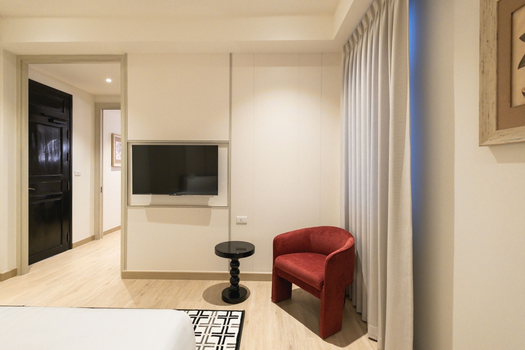 A modern living room with a flat-screen TV mounted on the wall, a small round table, and a red armchair.