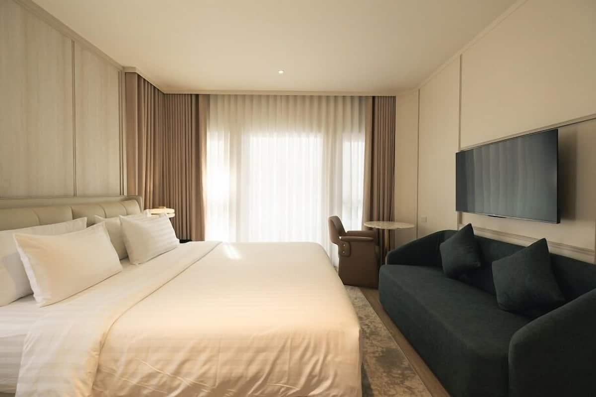 A hotel room with a large bed, a sofa, a TV, and a window with curtains.