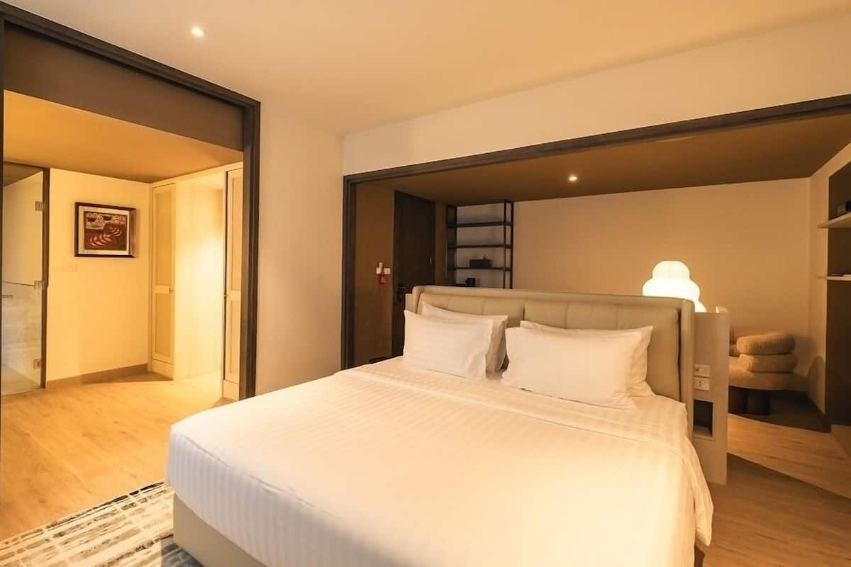 A modern hotel room with a large bed, a bedside table, a chair, and a wardrobe.