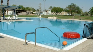 A swimming pool with a diving board, a red inflatable float, and a small orange ball.