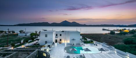 A modern building with a swimming pool and outdoor seating area, overlooking a body of water and mountains.