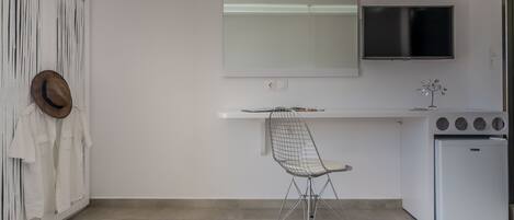 A modern kitchen with a white countertop, a built-in TV, a small fridge, and a wire chair.