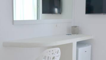 A white desk with a flat-screen TV mounted above it, a small trash bin, and a white chair.