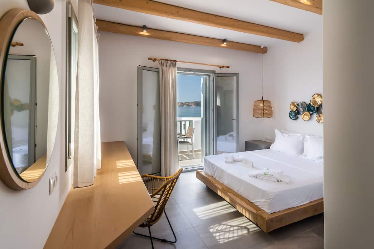 A bedroom with a bed, a chair, a mirror, and a view of the outside.