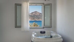 Un baño con bañera de hidromasaje, una ventana con vistas a la montaña y al mar, y una cortina.