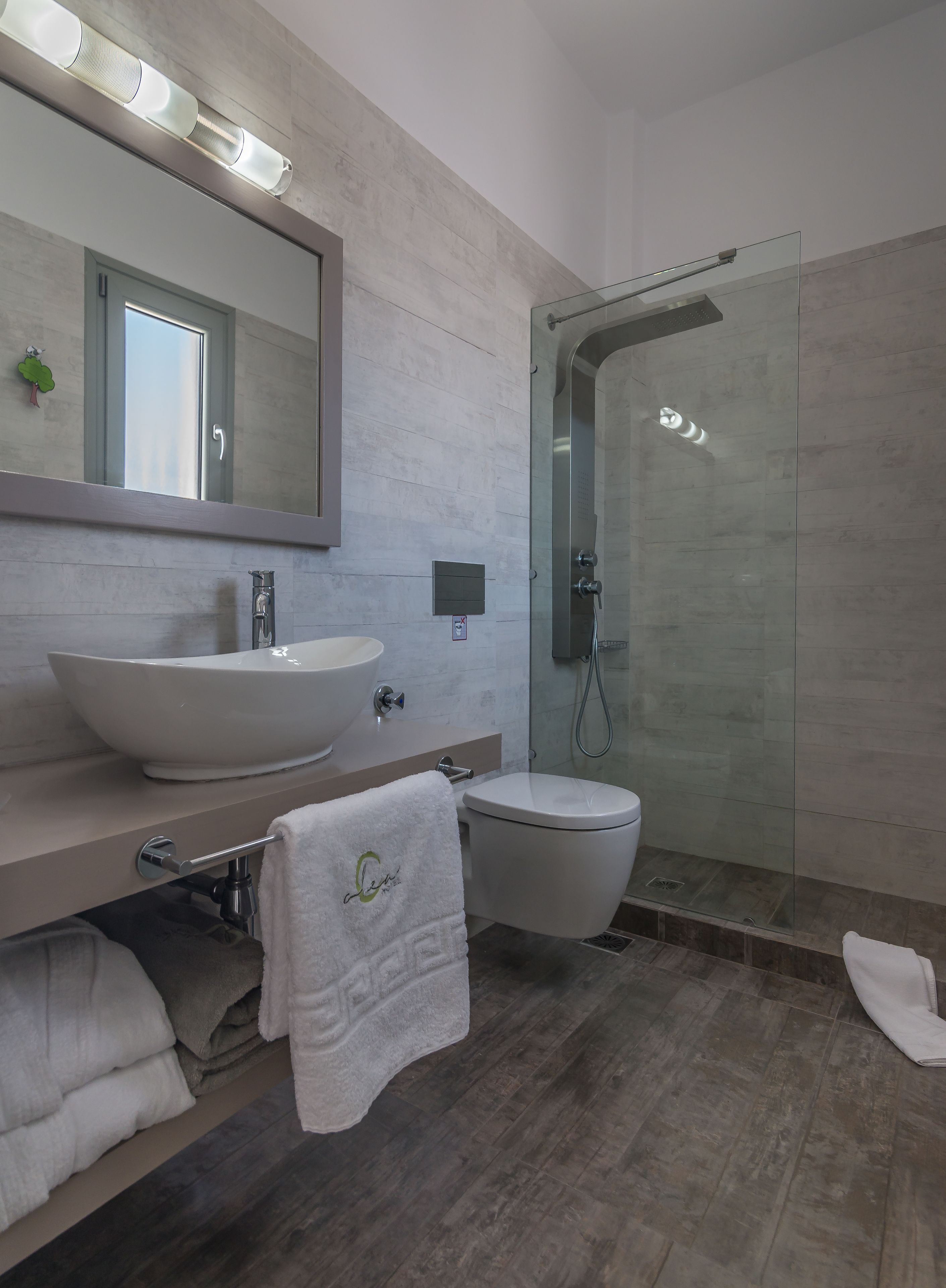 A modern bathroom with a large mirror, a white sink, a toilet, and a glass-enclosed shower.