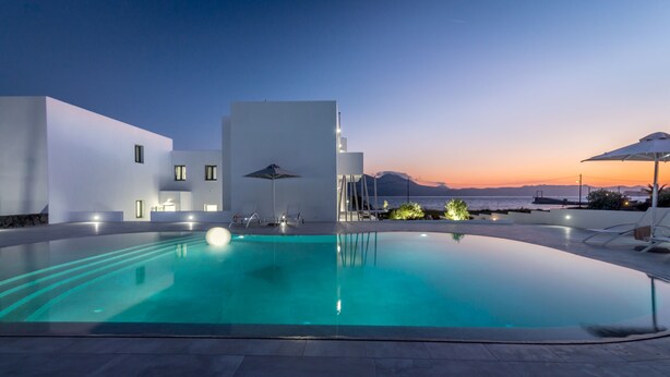 Un área de piscina moderna con vista despejada al mar y a las montañas al atardecer.