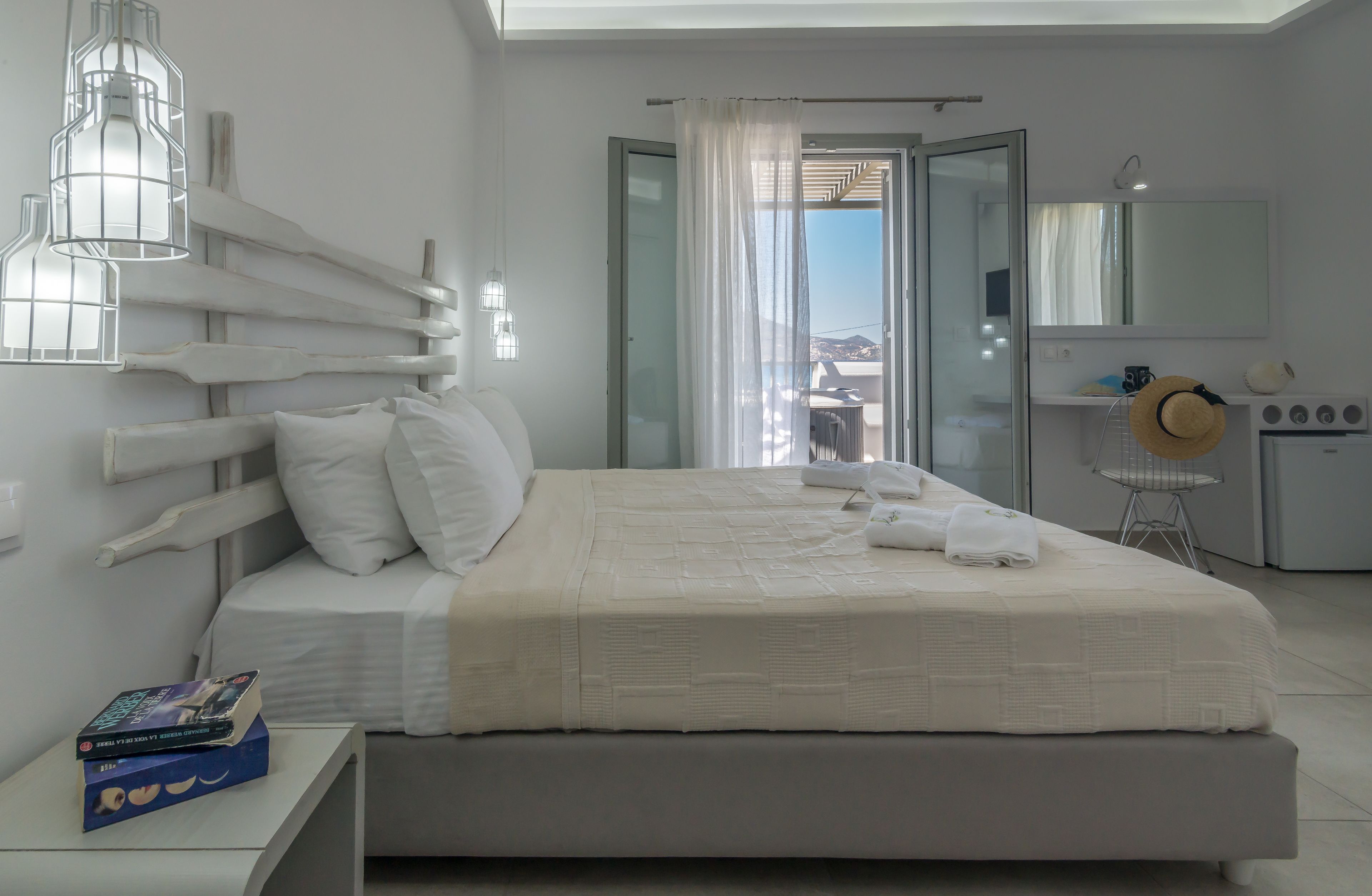 Un dormitorio moderno con una cama grande, una mesita de noche con un libro, y un baño visible a través de una puerta abierta.