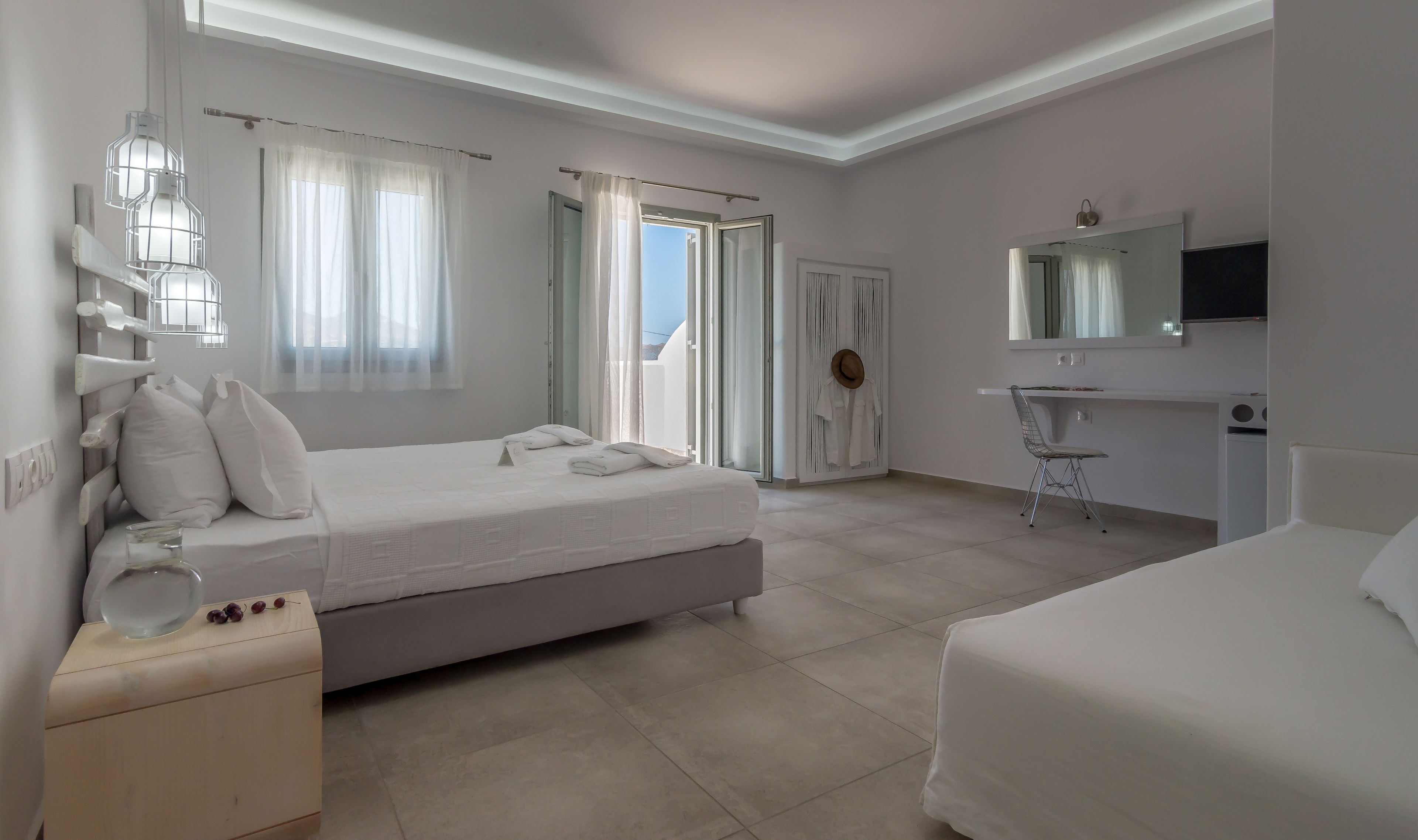 A modern hotel room with a large bed, a bedside table, a chair, a TV, and a bathroom with a shower and toilet.