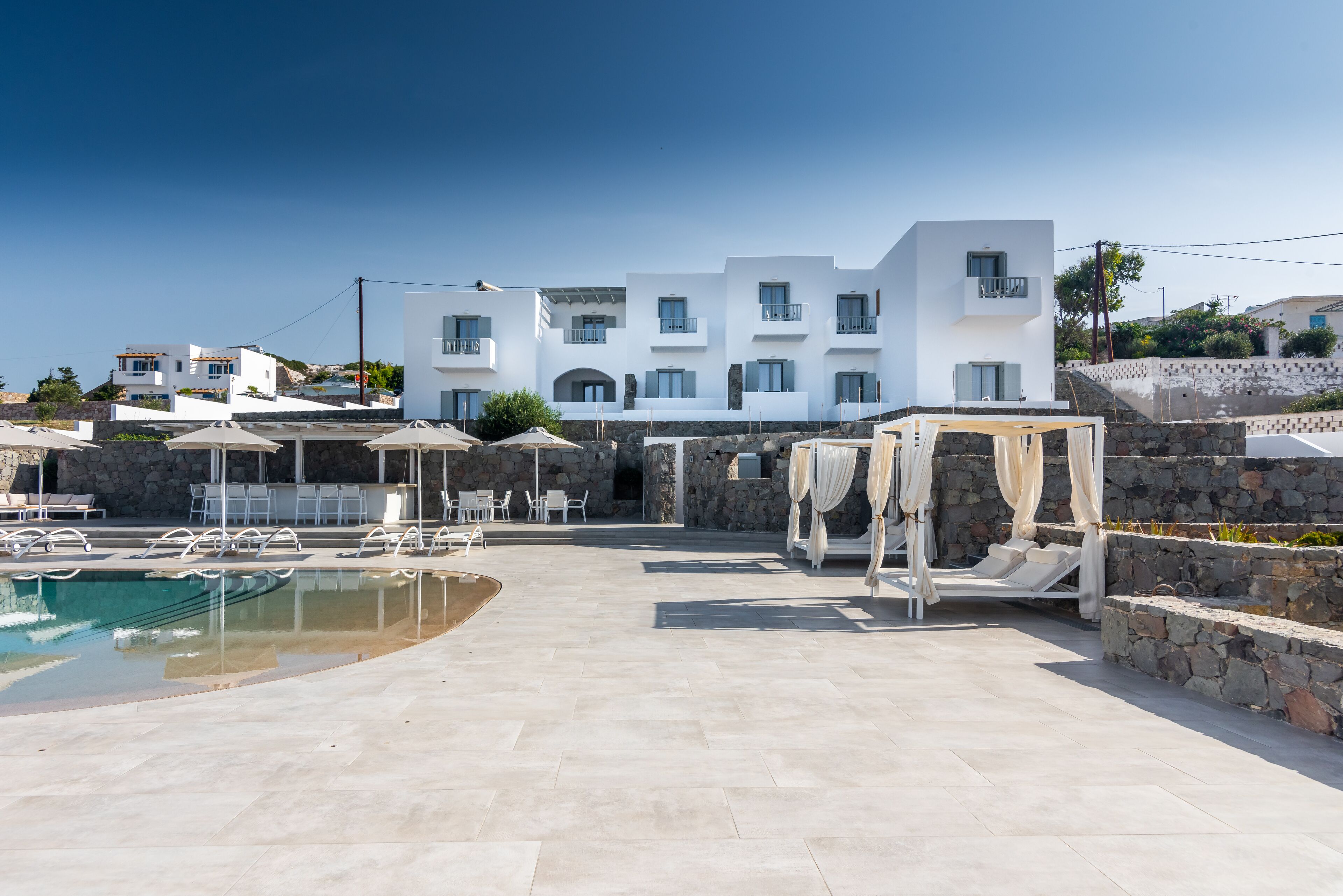 A modern hotel with a pool, outdoor seating, and a stone wall.