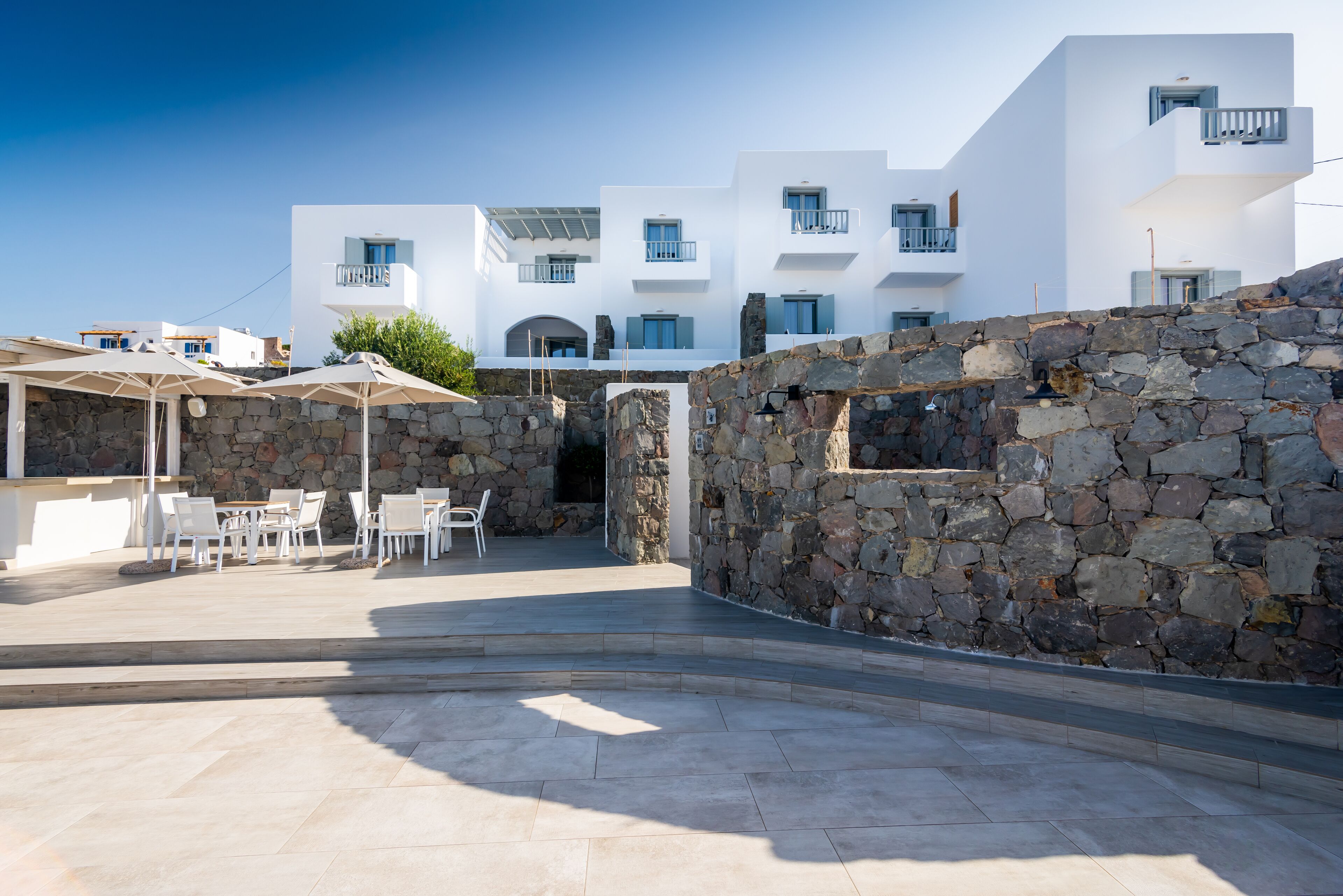 A modern building with white exterior walls, stone walls, and a patio area with outdoor seating.