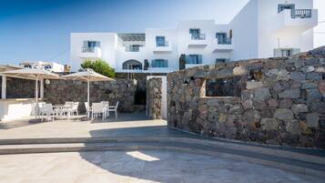 A modern building with white exterior walls, stone walls, and a patio area with outdoor seating.