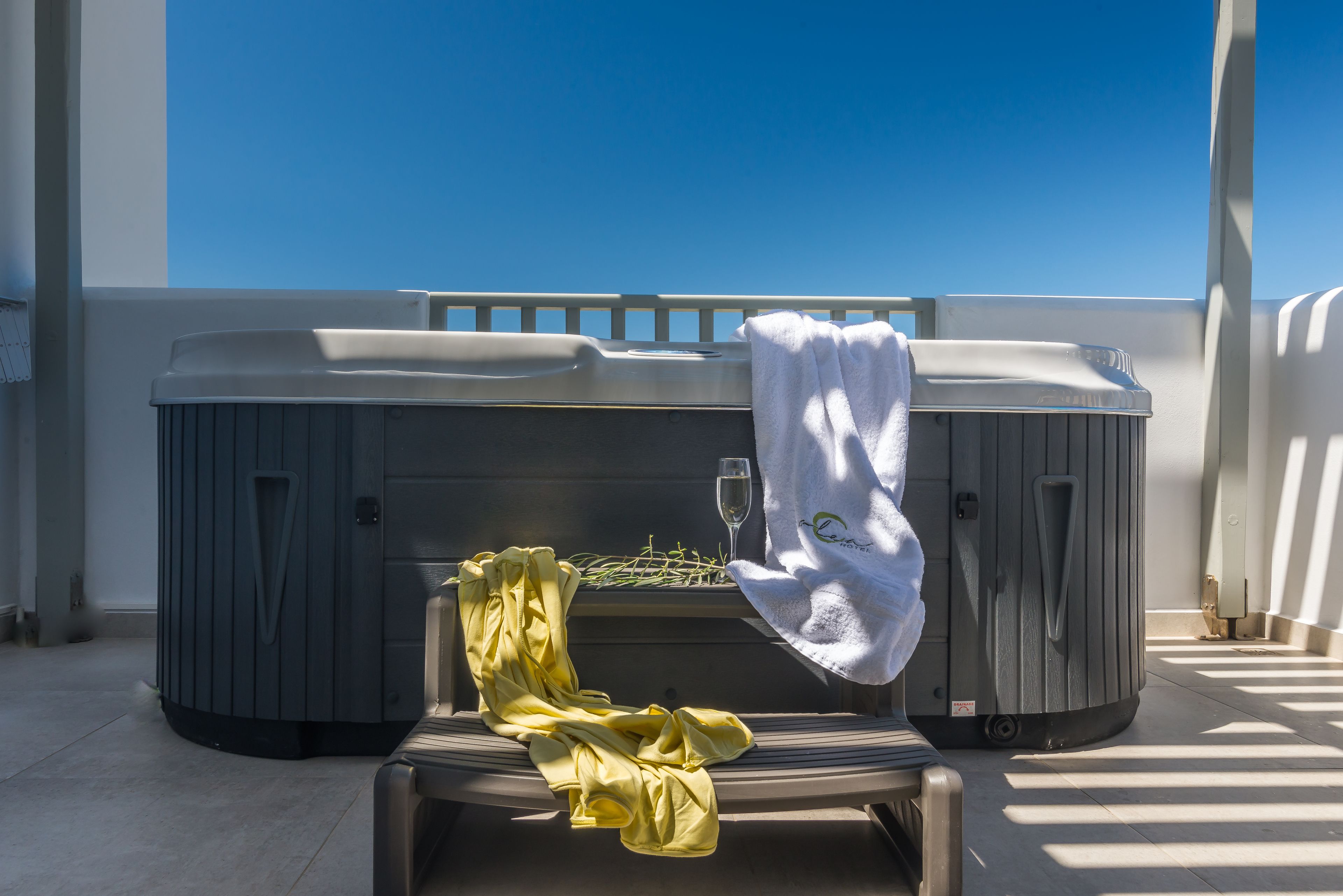 Un jacuzzi con una toalla y una copa de vino en un balcón, con un cielo azul despejado de fondo.