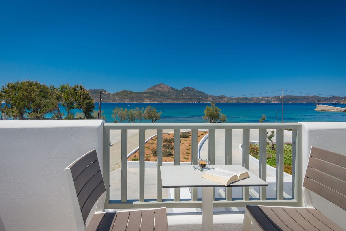 A balcony with a view of the sea, a table with a book, and a chair.
