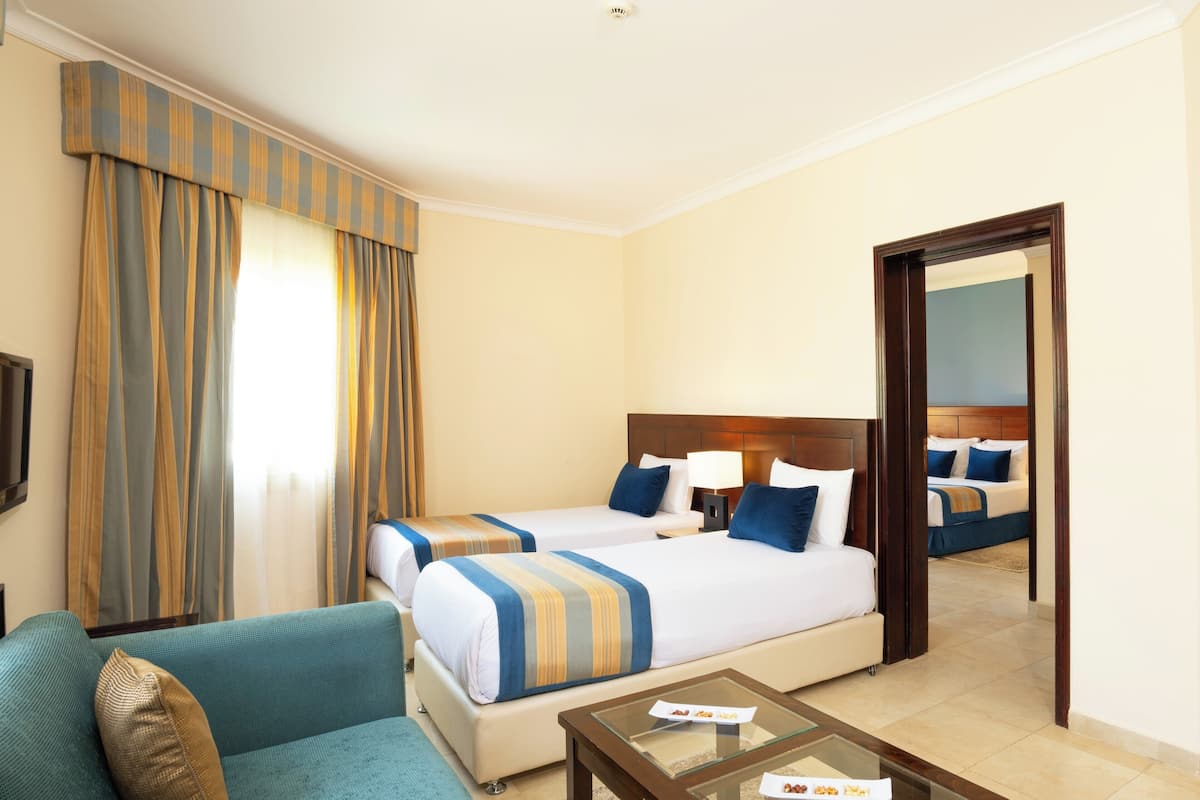 A hotel room with two beds, a sofa, a coffee table, and a large mirror.