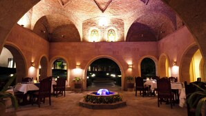 Un comedor interior con arcos de ladrillo, mesas, sillas y una fuente central.