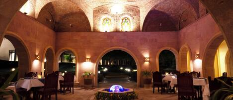 An indoor dining area with brick arches, tables, chairs, and a central fountain.