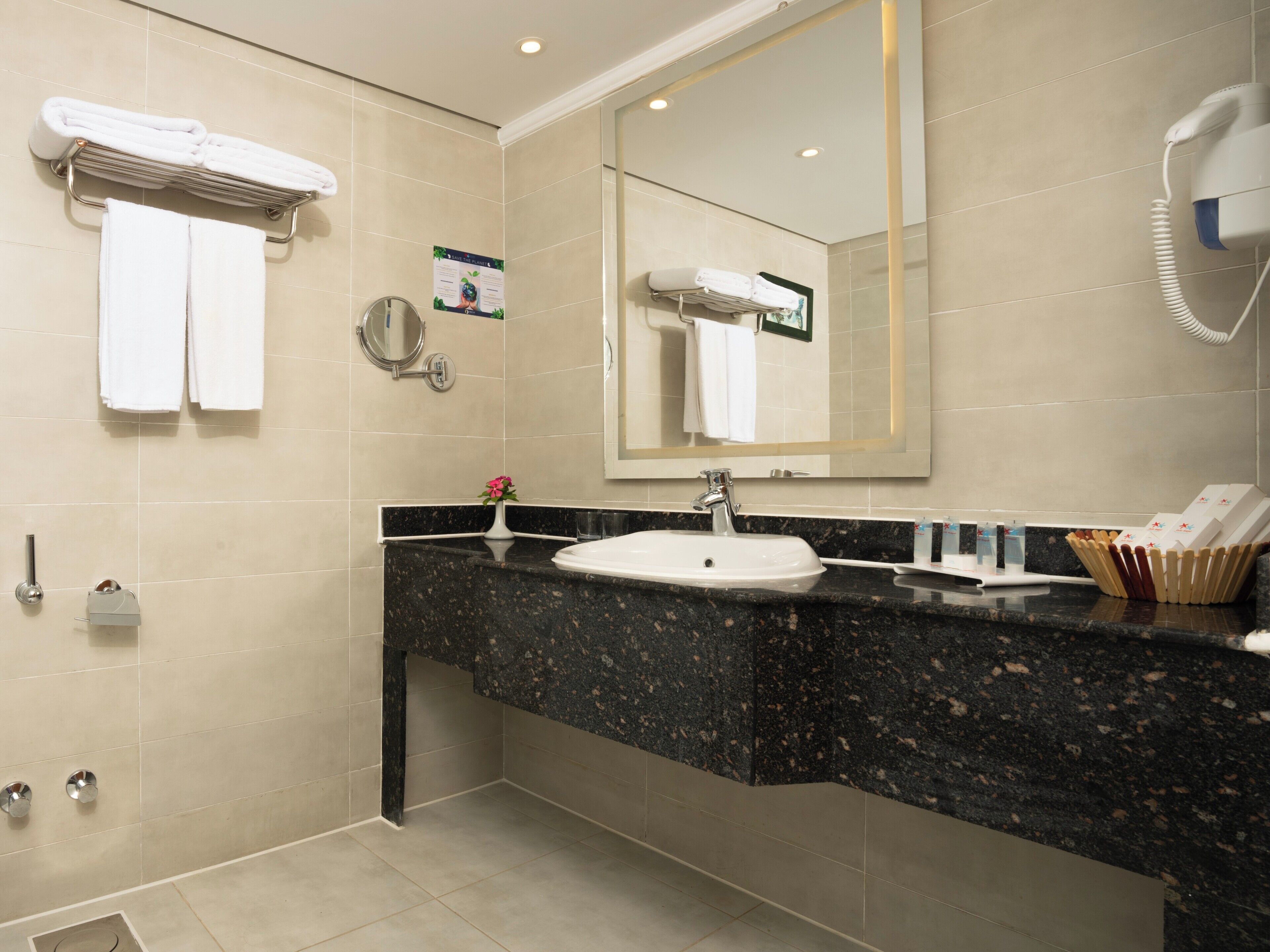 A modern bathroom with a granite countertop, a white sink, and a hairdryer mounted on the wall.
