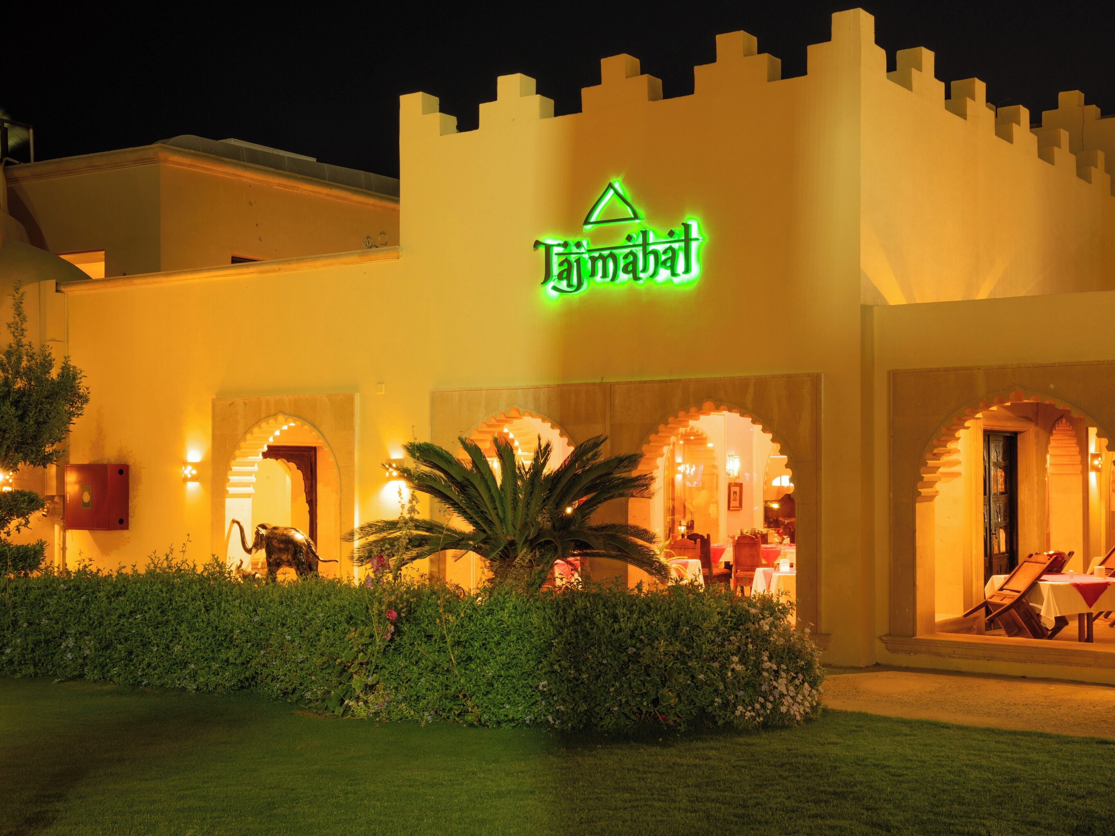 A hotel with a castle-like facade, illuminated signage, and a well-maintained garden.