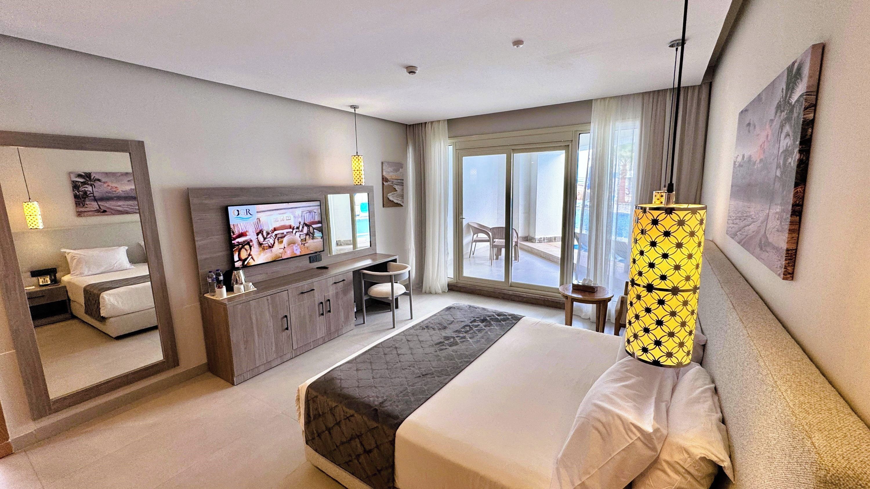 Une chambre d’hôtel comprenant un lit, une télévision, un bureau, une chaise, une lampe, une fenêtre avec vue et un tableau au mur.