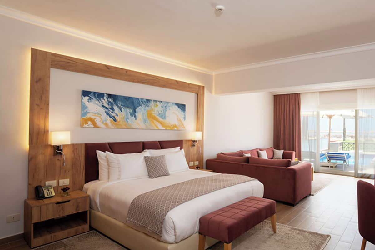 A modern hotel room with a large bed, a sofa, and a view of the sea.