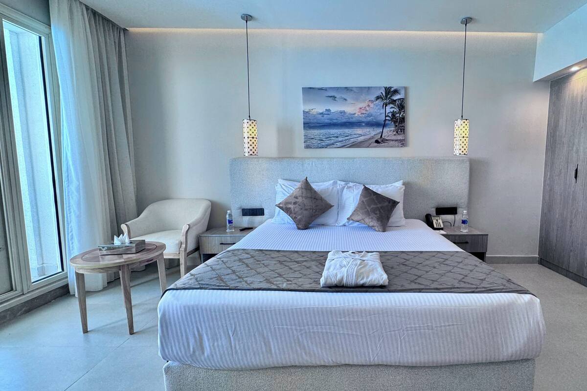 A modern hotel room with a large bed, a chair, a small table, and a painting on the wall.