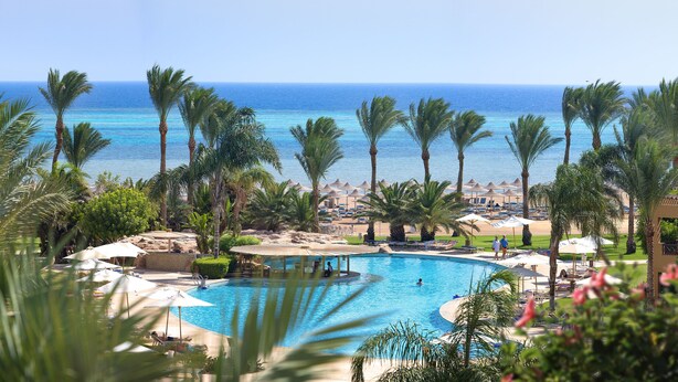 Piscina de resort con palmeras, una playa y vista al océano.