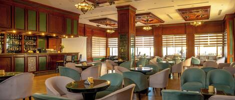 Een ruime lobby met een bar, comfortabele zitplaatsen en decoratieve elementen aan het plafond.