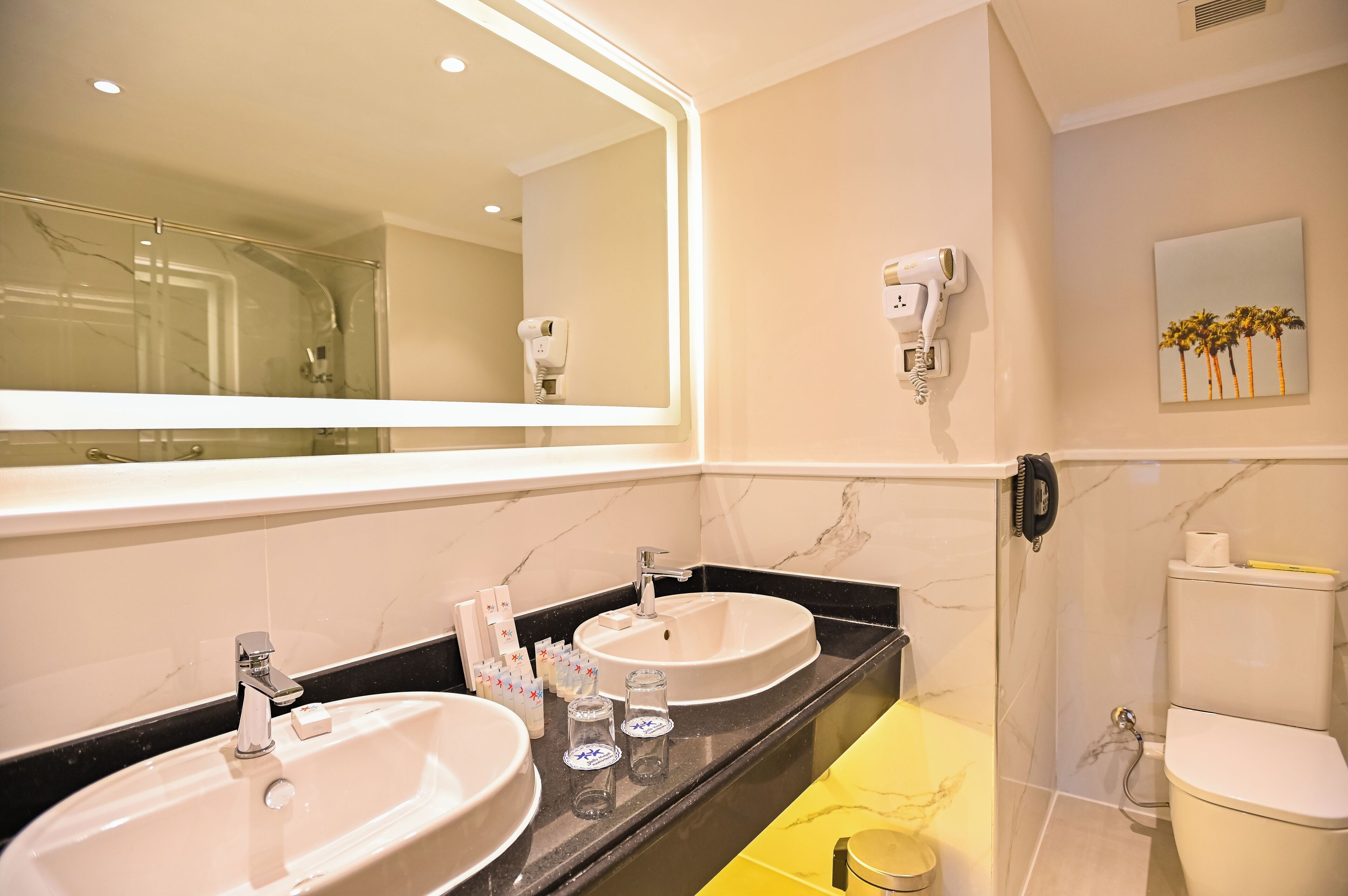 A bathroom with two sinks, a large mirror, a hairdryer, and a toilet.