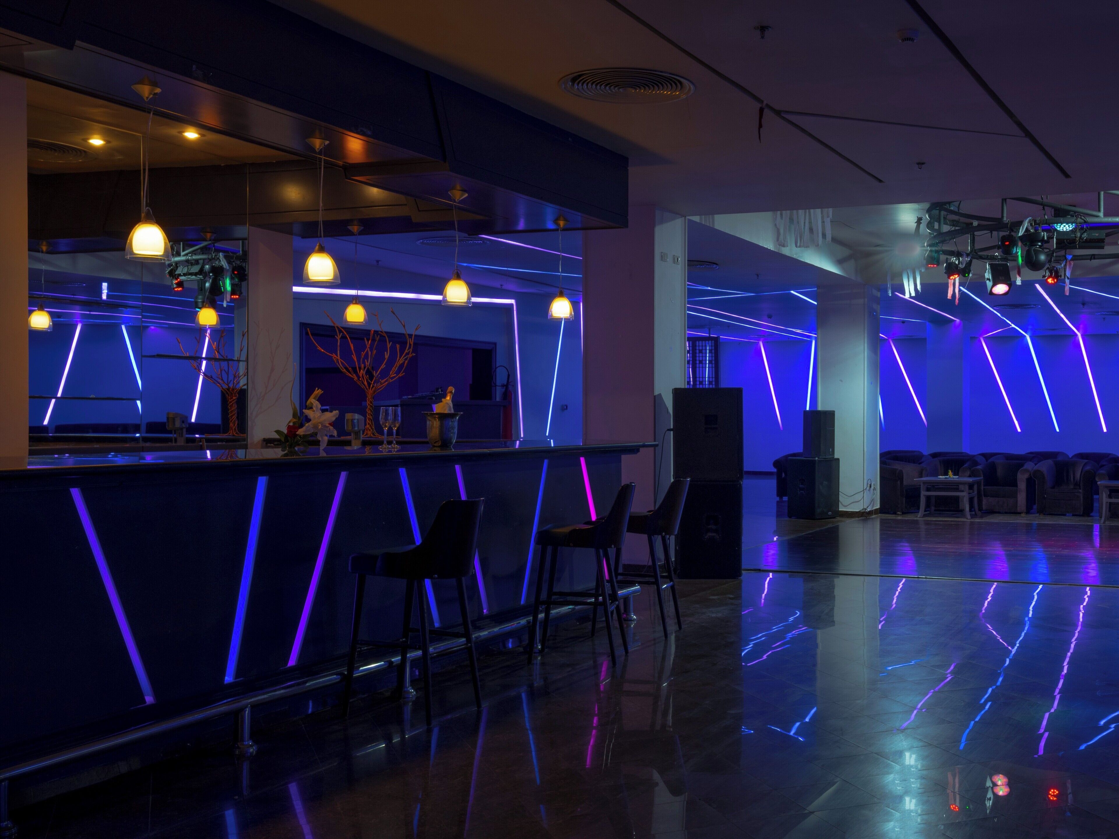 A modern bar area with a sleek design, featuring a bar counter, seating, and ambient lighting.