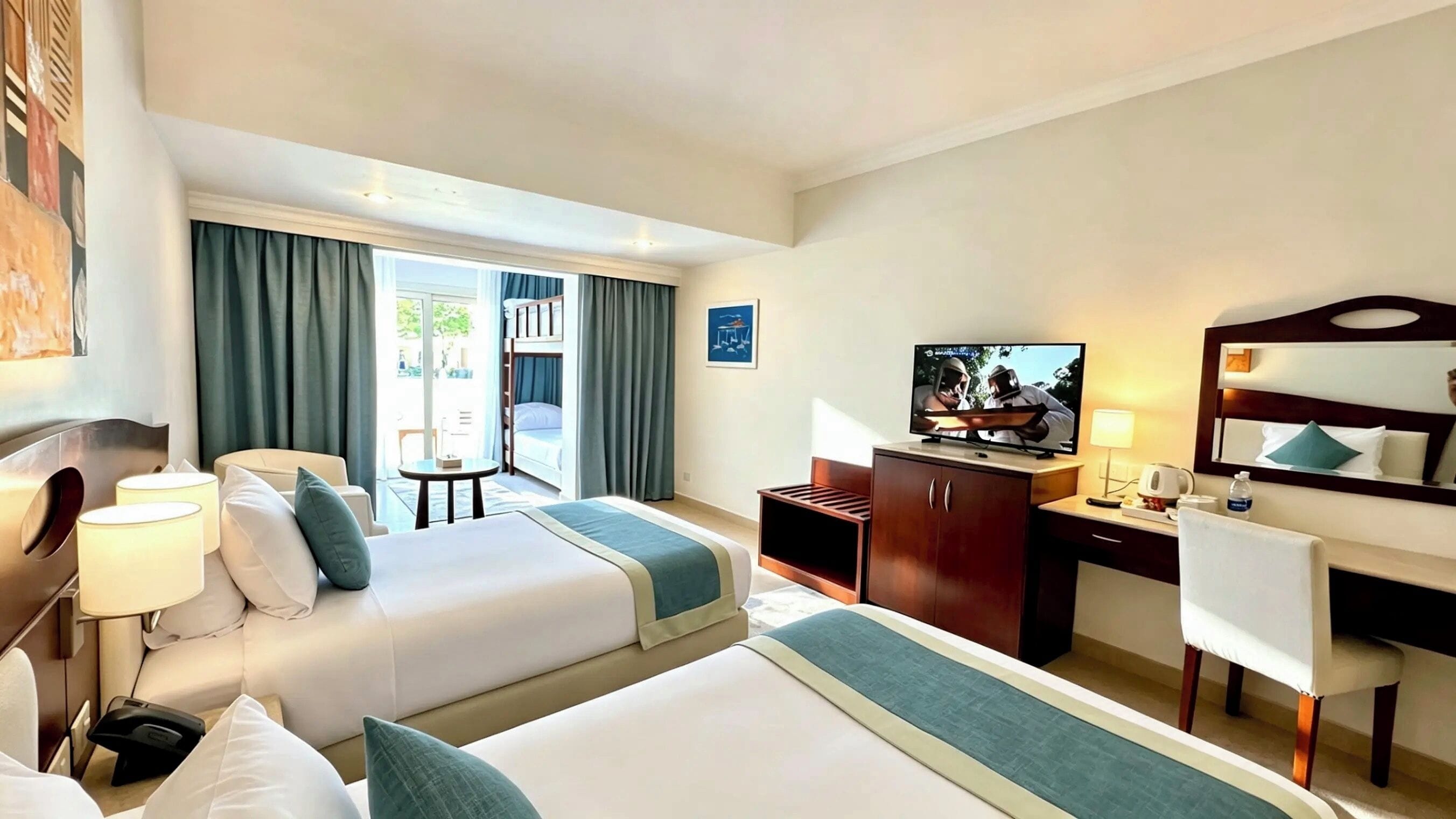 Quarto de hotel com duas camas, uma escrivaninha, televisão e varanda com cortinas.