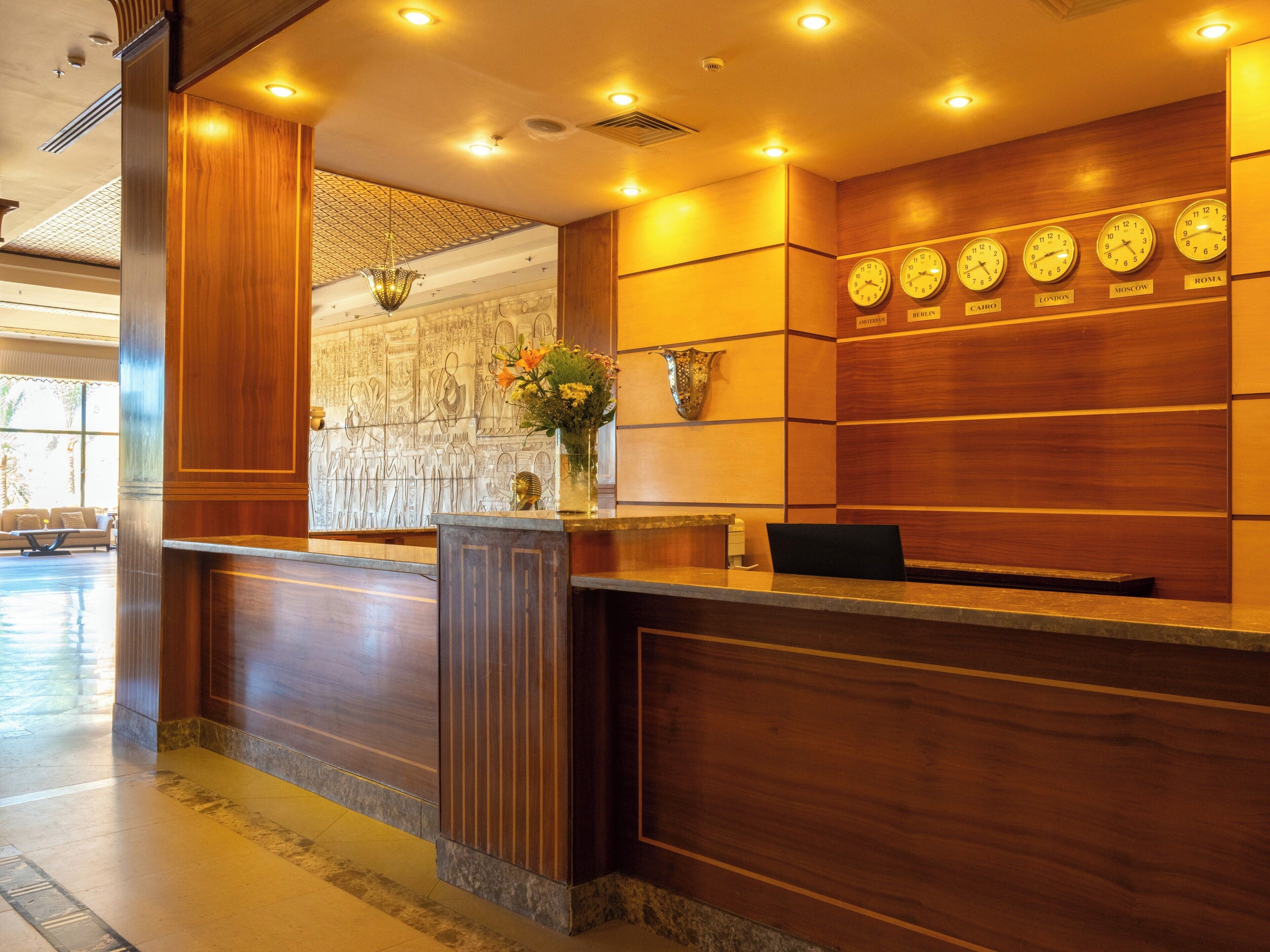 A reception desk with clocks displaying times from various cities, a vase with flowers, and a wall with Egyptian hieroglyphs.