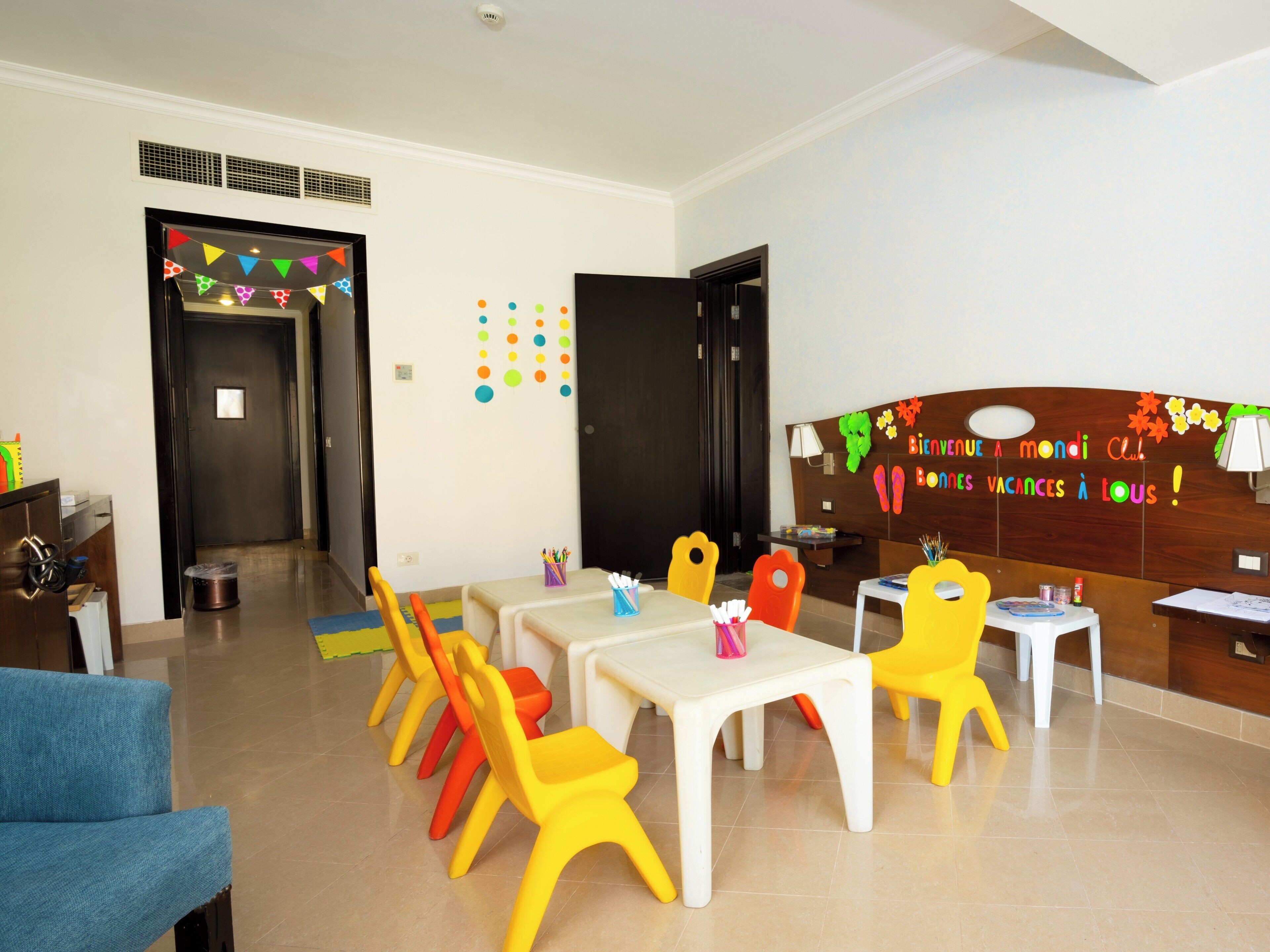 A brightly colored children's play area with a long table and chairs, a blue sofa, and a wall with colorful decorations.