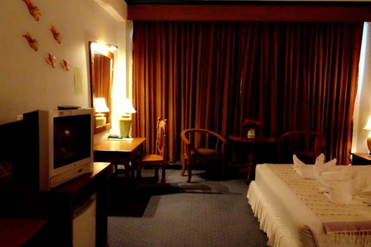 A hotel room with a bed, a television, a desk with a lamp, and a chair.