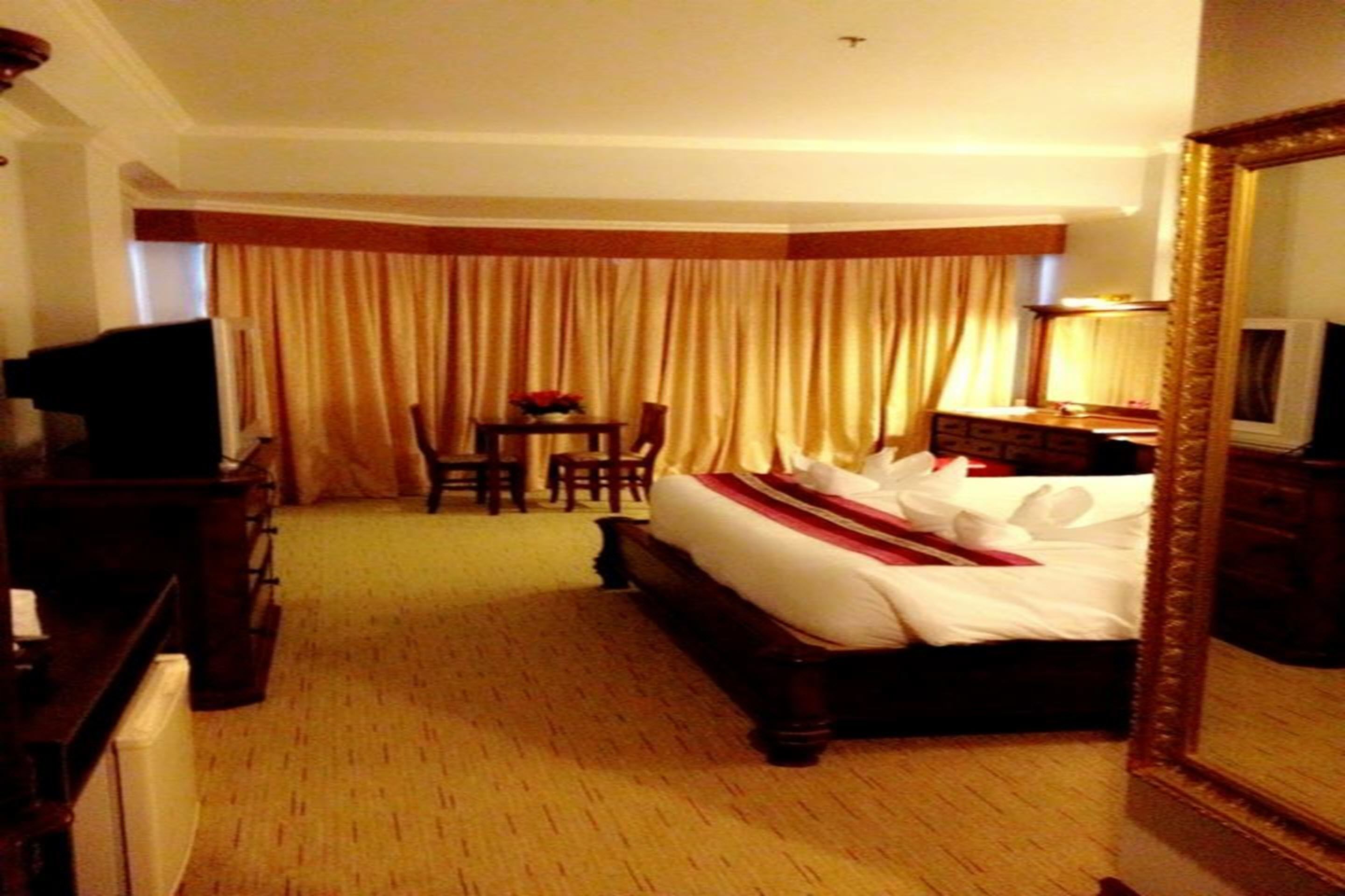 A hotel room with a large bed, a desk, a chair, a TV, and a mirror.