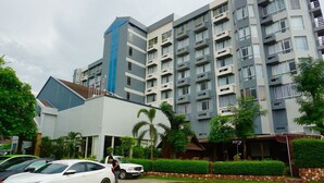 Un hotel de varios pisos con un diseño moderno, que cuenta con balcones y un estacionamiento con coches.