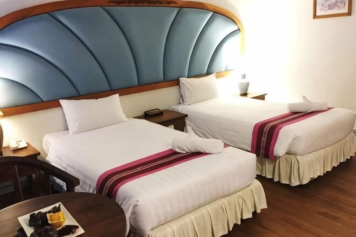 A hotel room with two beds, a wooden headboard, bedside tables, and a small table with fruit.