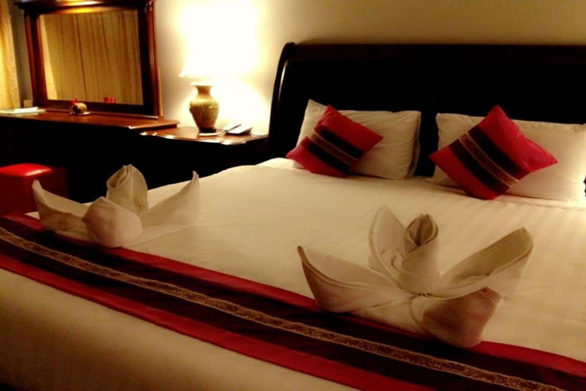 A hotel room with a neatly made bed, red and white pillows, and a red and white striped bed runner.
