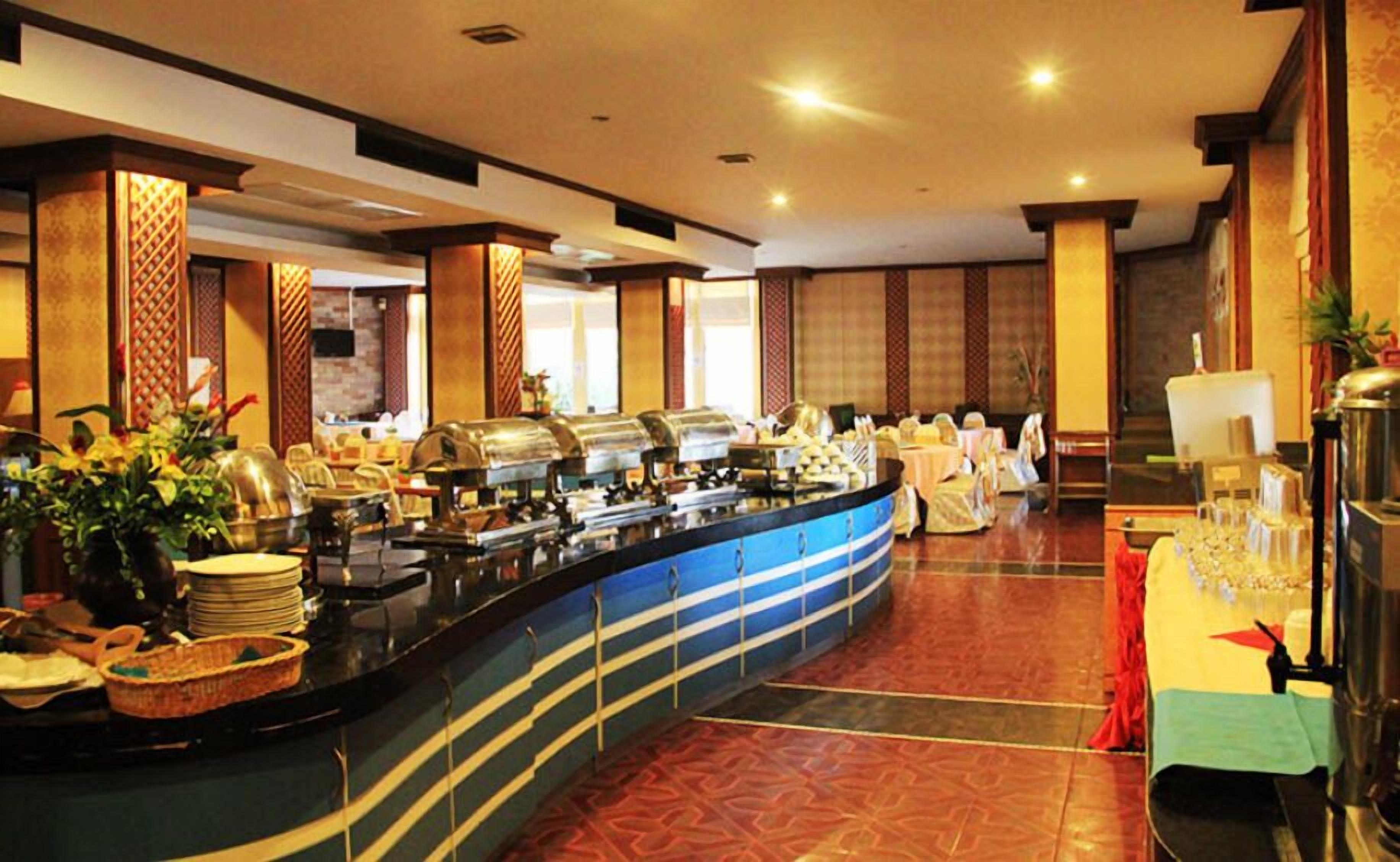 A buffet area with multiple food stations, a counter with stacked plates, and a table with glasses and a pitcher.