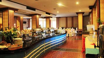 A buffet area with multiple food stations, a counter with stacked plates, and a table with glasses and a pitcher.