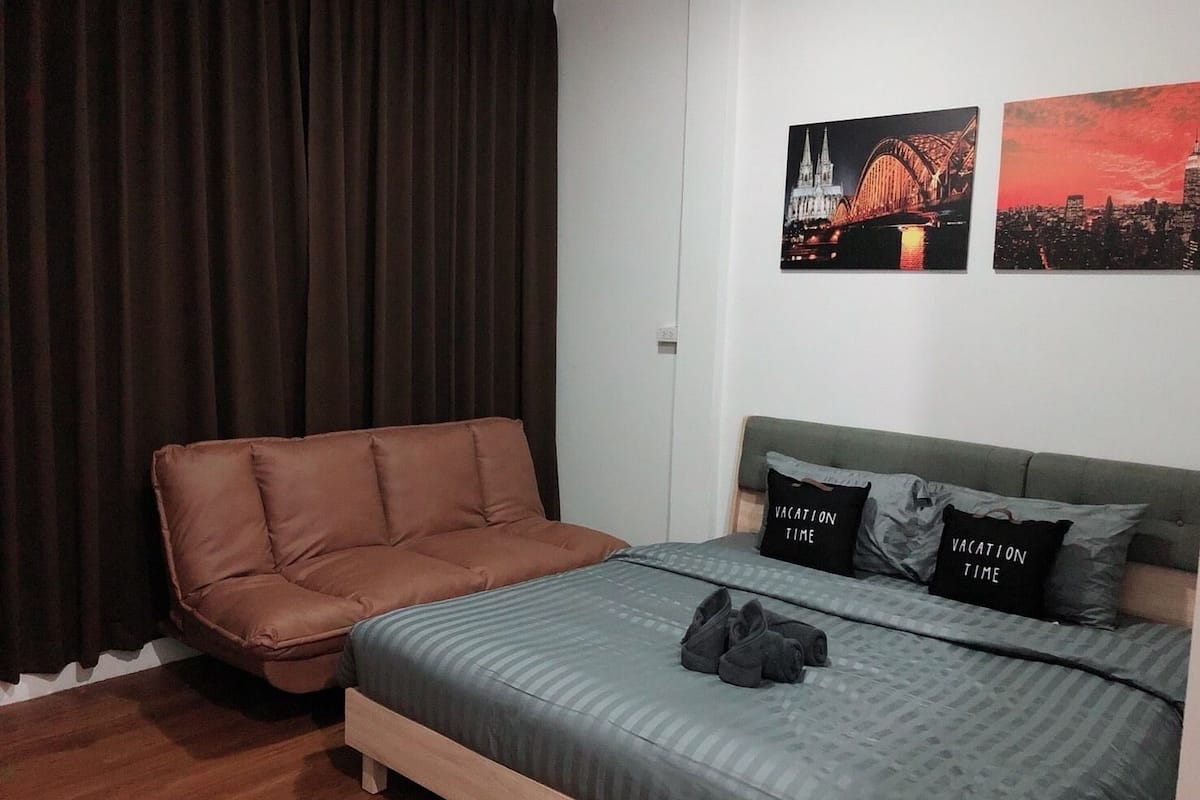 A bedroom with a bed, a brown sofa, and two wall art pieces depicting bridges.