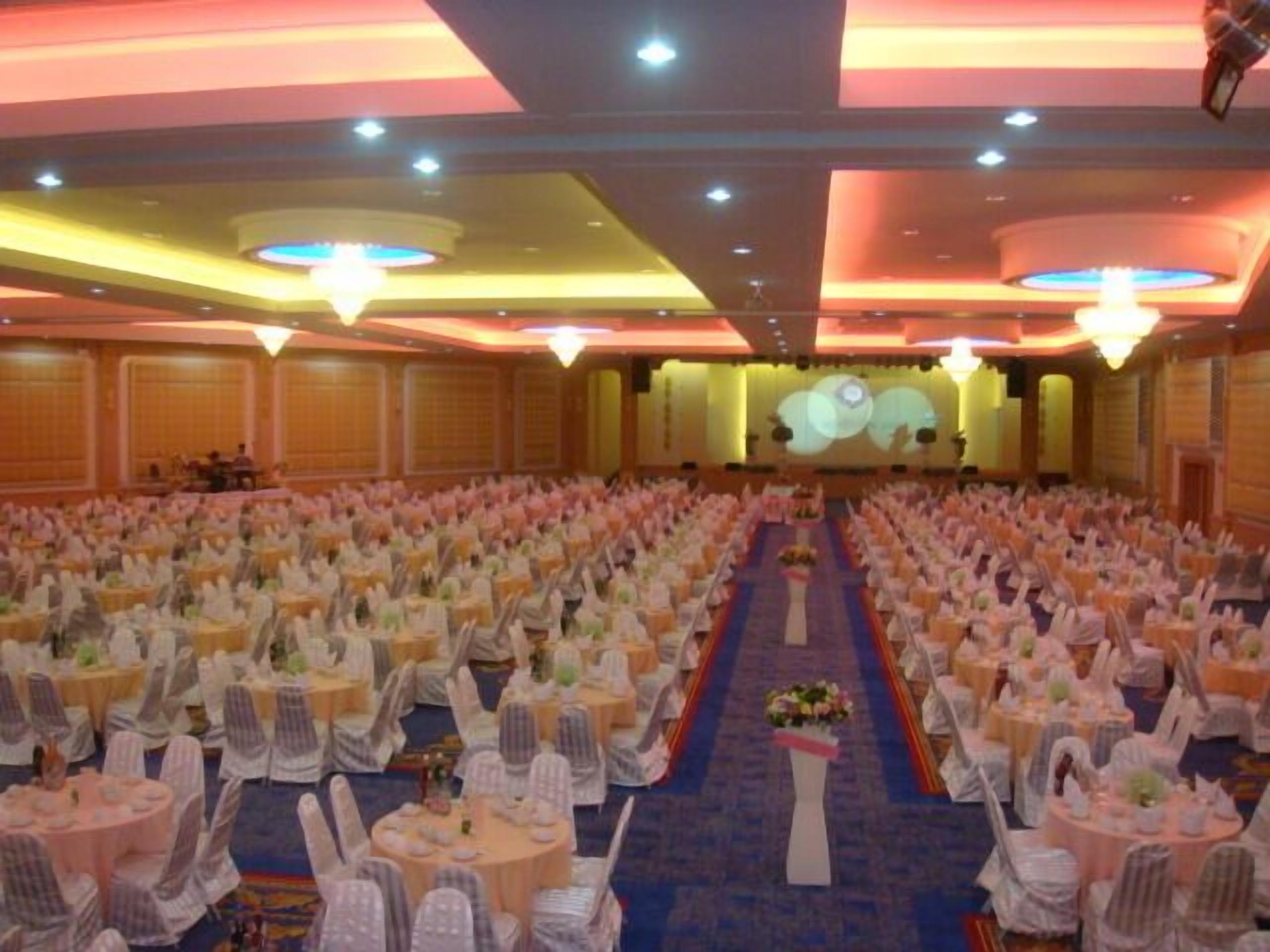A large hall with rows of tables and chairs, a stage at the front, and a carpeted floor.
