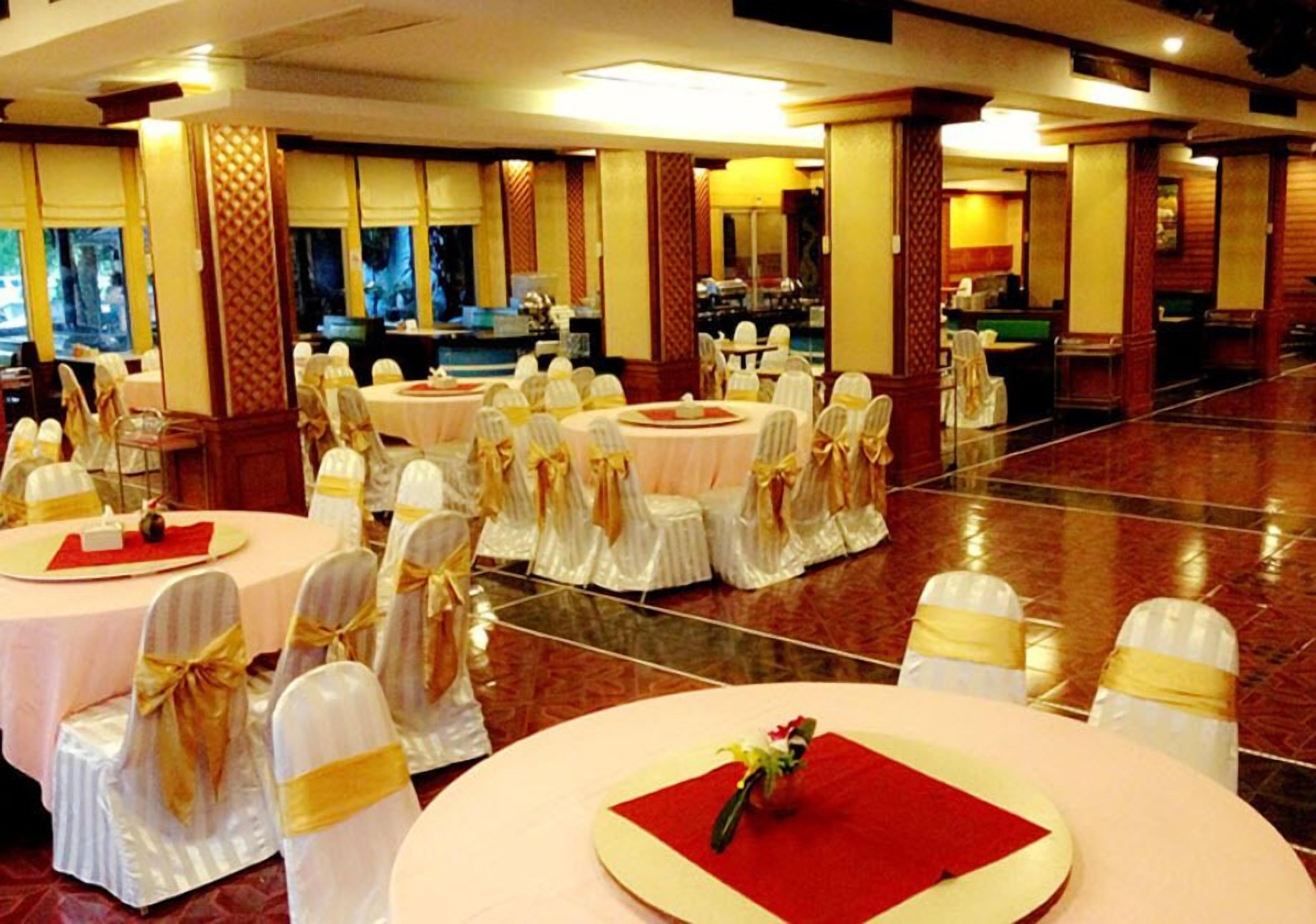 Un salón de banquetes con mesas redondas, sillas blancas con cintas doradas y una alfombra roja.