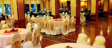 Un salón de banquetes con mesas redondas, sillas blancas con cintas doradas y una alfombra roja.