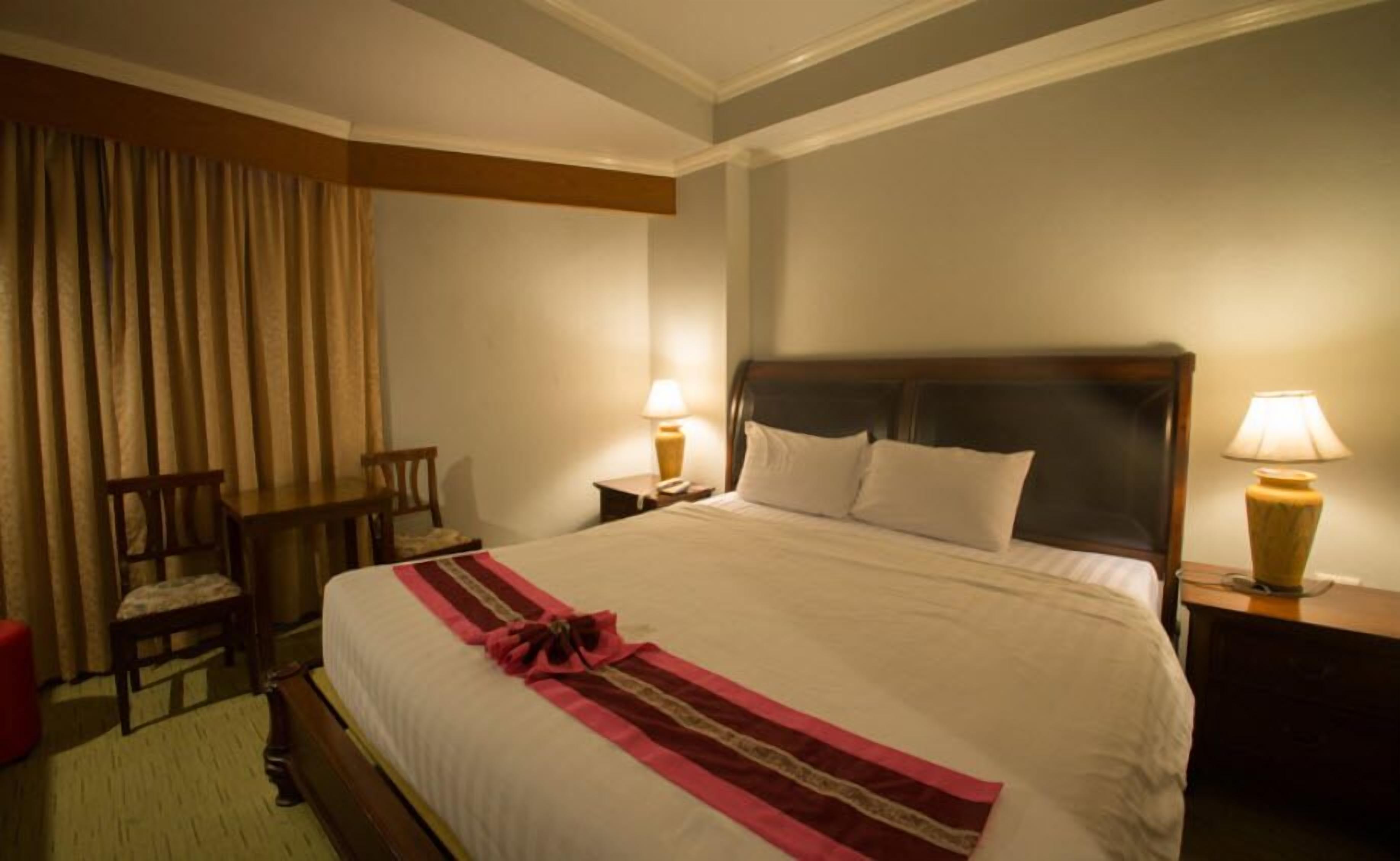 A hotel room with a large bed, two bedside tables with lamps, a chair, and a window with curtains.