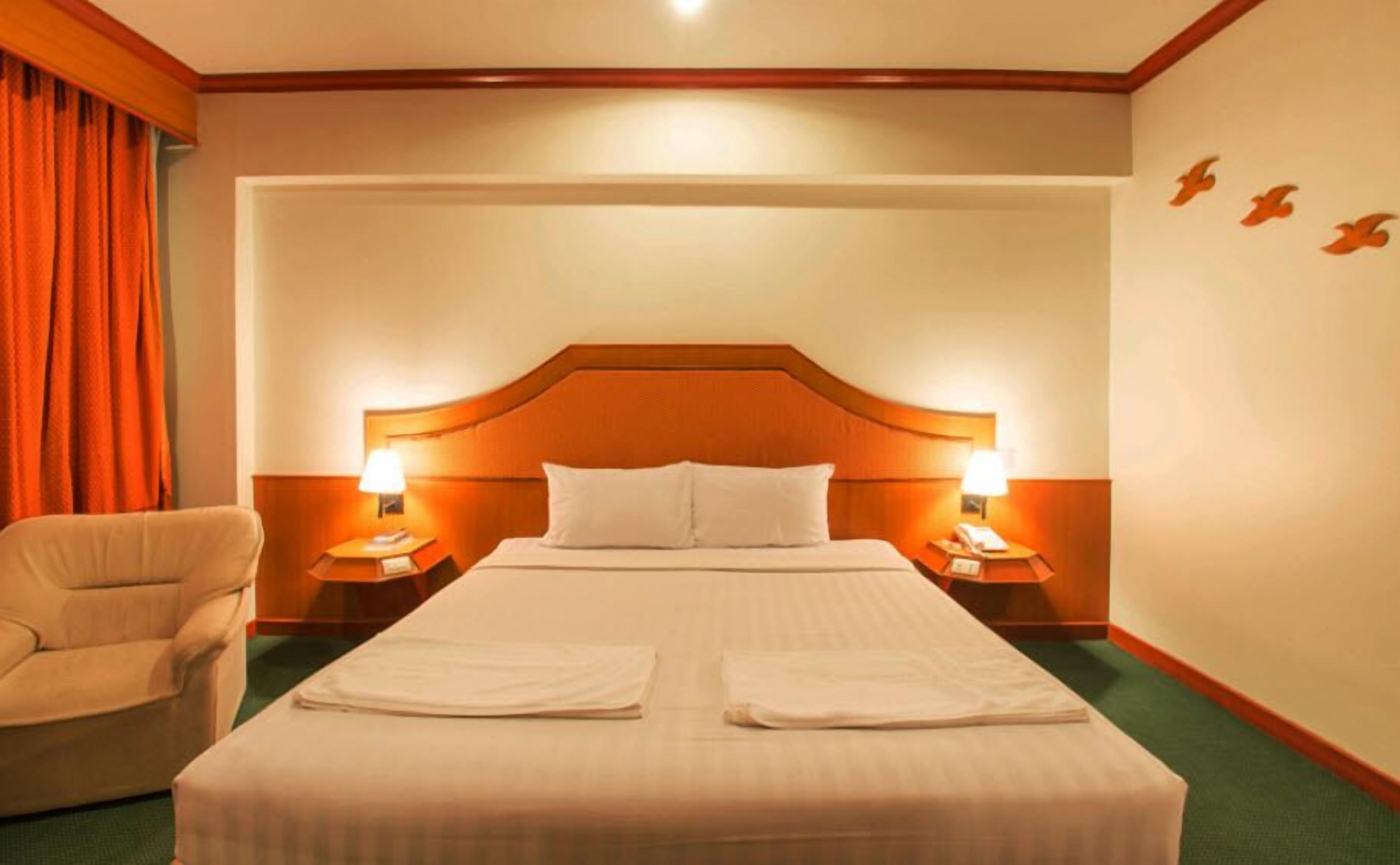 A hotel room with a large bed, two bedside tables with lamps, a chair, and a curtain.