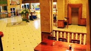 Un hall con suelo de baldosas, un arreglo floral central y una zona de estar con barandilla de madera.