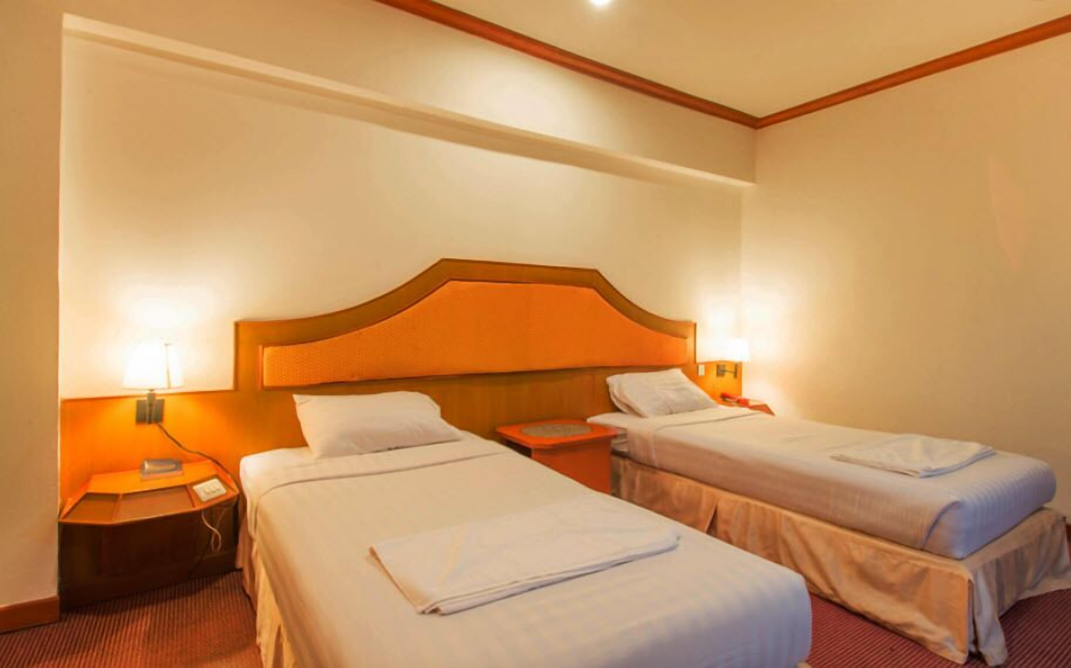 A hotel room with two single beds, a wooden headboard, bedside lamps, and a nightstand with a phone and charger.