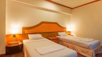 A hotel room with two single beds, a wooden headboard, bedside lamps, and a nightstand with a phone and charger.